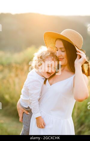 Cheerful mother in a straw hat with a cute curly-haired boy in her arms Stock Photo