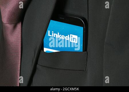 LinkedIn on cellular phone. Professional networking, blue logo on smartphone screen. Online job search and job offers in app. Business suit pocket. Stock Photo