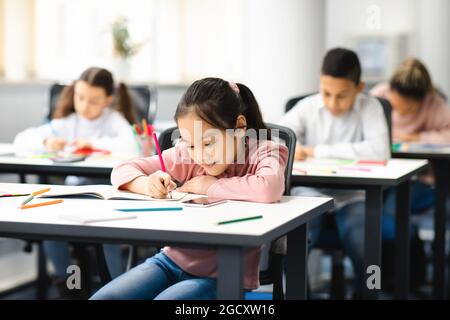 Portrait of diverse schoolchildren sitting in classroom writing and drawing Stock Photo
