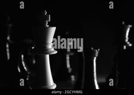 White Chess Queen piece in Black and White Close up surrounded by black pieces, cast in shadow Stock Photo