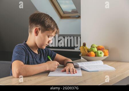 Kid boy doing homework at kitchen table with book Stock Photo