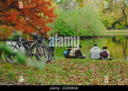 parked bicycles in autumn park and group of people near pond in city park in a rainy autumn day, horizontal photo Stock Photo