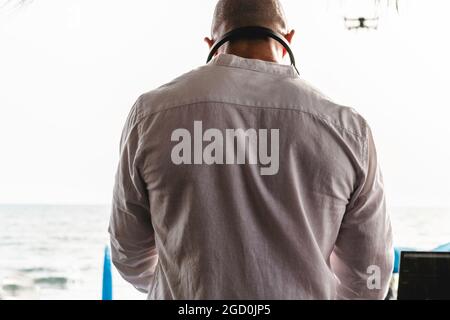 Back view of drone pilot flying with quadcopter outdoors at sunset - Drone pilot flying and commanding from the beach - Technology and spying concept Stock Photo