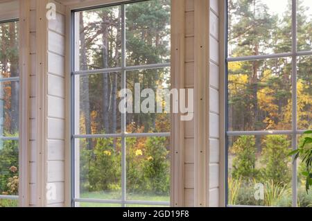 Bright interior of the room in wooden house with a large window overlooking the autumn courtyard. Golden autumn landscape in white window. Stock Photo