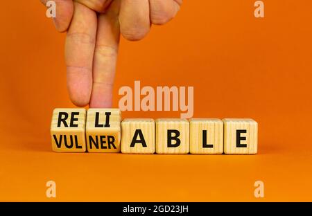 Vulnerable or reliable symbol. Businessman turns wooden cubes and changes the word Vulnerable to Reliable. Beautiful orange background, copy space. Bu Stock Photo