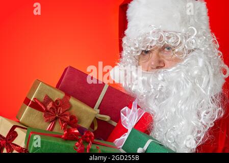 Happy Santa Claus with gift boxes in hands on red background with copy space Stock Photo