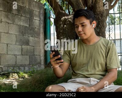 Young latino man using his smart phone and wireless headphones Stock Photo