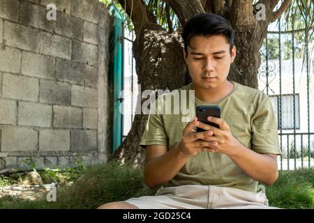 Young man using his smart phone sitting on the grass Stock Photo