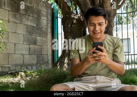Cheerful young man using his smart phone sitting on the grass Stock Photo