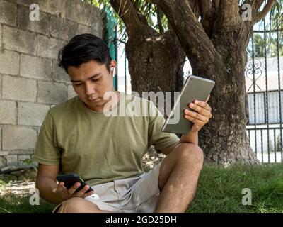 A young man holding a tablet while checking his smart phone Stock Photo