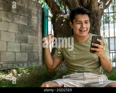 Exalted latin young man using his smart phone sitting Stock Photo