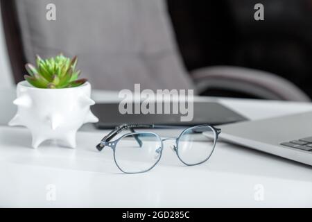 Stylish blue male glasses for vision on desktop with laptop graphics tablet and plant. Fe,ale Eyeglasses on workspace. Optics healthy vision for Stock Photo