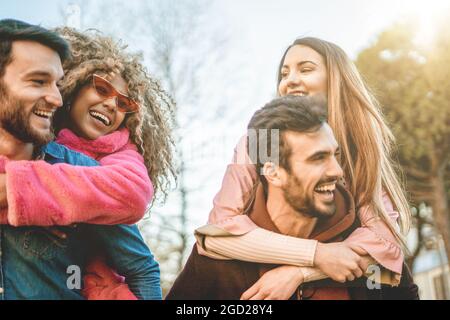 Interracial happy friends laughing having fun piggybacking outdoors - concept of young people friendship. Stock Photo