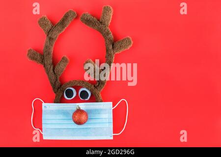 Christmas reindeer in face mask looking at gift box on red background. New year and Christmas during corona virus concept. Stock Photo