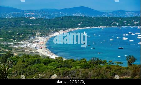 Panoramic view mediterranean sea bay with boats against blue summer sky and mountains background - Plage de pampelonne, St. Tropez (focus on lower thi Stock Photo