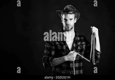 Lasso tool of American cowboy. Still used on ranches to capture cattle or other livestock. Western life. Man unshaven cowboy black background. Cowboy Stock Photo