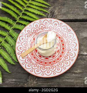 Eco friendly, food composition with organic, vegan, homemade yogurt with wooden spoon and fern leave on a wooden table. Dairy-free yogurt. Product for Stock Photo