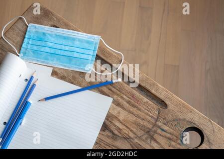 blue disposable face mask with open notebook to blank white page and blue pencil on vintage wood desk with copy space Stock Photo