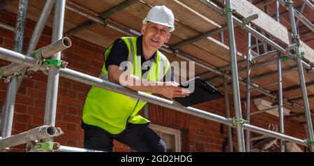 Panoramic web banner header of male builder foreman, construction worker, contractor or architect on building site writing on black clipboard panorama Stock Photo