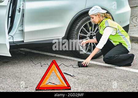 woman in an emergency vest inflates car wheel Stock Photo