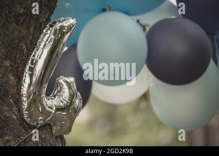 silver balloon number four tied to a tree with a rope and in the background still usually balloons in blue, gray and white as a children's party decor Stock Photo