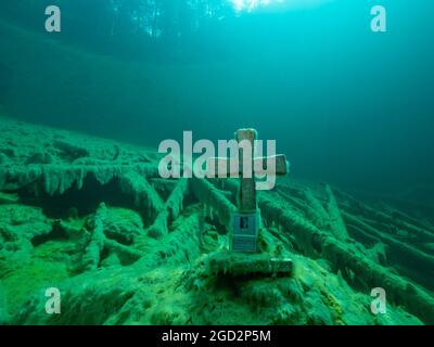 Stone cross underwater in a mountain lake, Good visibility, clear water and some tree trunks underwater, Reflection of a forest on the water surface, Stock Photo
