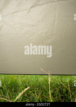 Rain drops on tent fabric flowing down into grass. Spend rainy day in dry tent. Stock Photo