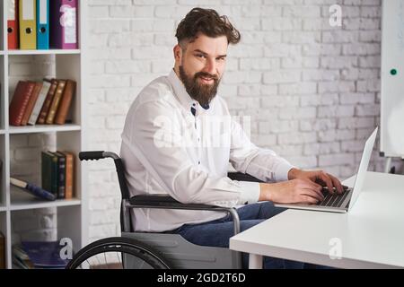 Portrait of a happy man working on a laptop and sitting on a wheelchair Stock Photo