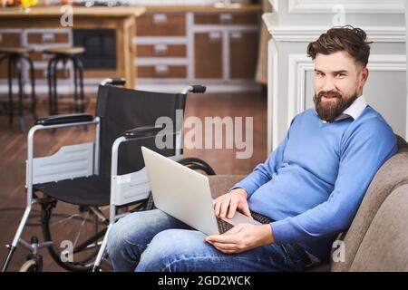 Disabled man sitting on a comfy couch and using a laptop Stock Photo