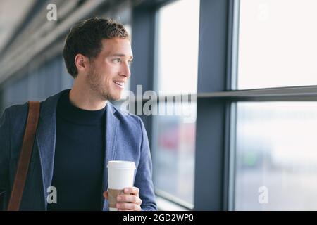 Businessman drinking coffee walking in airport. Casual urban professional smiling happy wearing suit jacket holding disposable coffee cup on travel Stock Photo