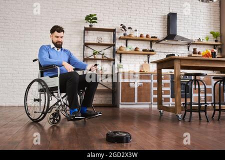 Man sitting in a wheelchair and using a robotic vacuum connected to his phone Stock Photo