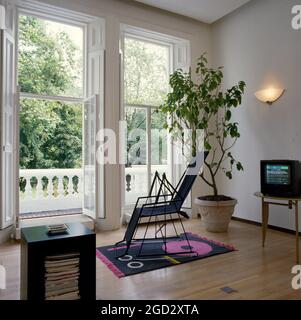 Designer livingroom with open french windows leading onto balcony with view of gardens beyond. Stock Photo