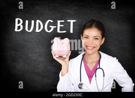 Health insurance cost during coronavirus pandemic healthcare professional Asian doctor woman showing piggy bank money savings on blackboard background Stock Photo