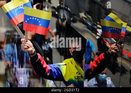 Caracas, Venezuela. 10th Aug, 2021. A member of Venezuela's Olympic team waves flags out the window as the team rides a bus through the city after arriving from Tokyo. Credit: Jesus Vargas/dpa/Alamy Live News Stock Photo