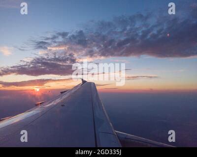 SUNSET ABOVE THE SKY VIEWED INFLIGHT FROM AN AIRPLANE WINDOW WITH THE WING IN THE FOREGROUND Stock Photo