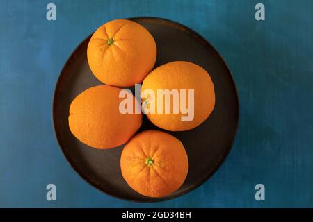 A bowl or platter of vibrant navel oranges on a bright blue textured background Stock Photo