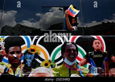 Caracas, Venezuela. 10th Aug, 2021. A man waves a small Venezuelan flag through the window of a bus with pictures of athletes from the Olympics printed on it. Credit: Pedro Rances Mattey/dpa/Alamy Live News Stock Photo