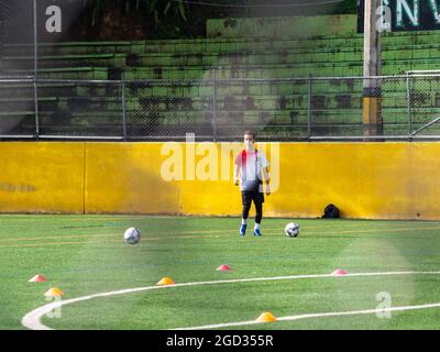 Medellin, Colombia - July 30 2021: Young Latin Teenager is Training with two Soccer Balls on a Green Synthetic Field in a Sunny Day Stock Photo