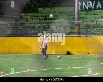 Medellin, Colombia - July 30 2021: Young Latin Teenager is Training with two Soccer Balls on a Green Synthetic Field in a Sunny Day Stock Photo