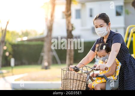 Mother with her child in masks going home on the bike during the pandemic Stock Photo