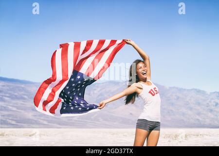 USA flag happy American Asian sports athlete woman waving after game winning cheering at outdoor landscape summer nature. Stock Photo