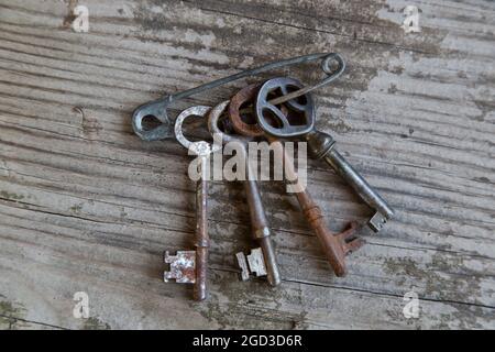 Classic metal keys held with a safety pin, hanging against a wood wall. Stock Photo
