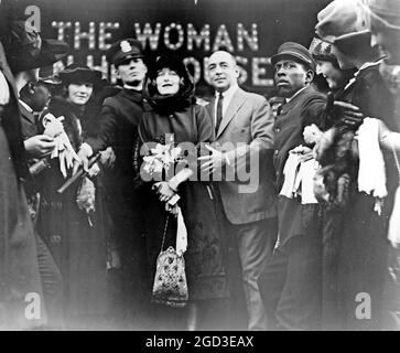 Mildred Harris Chaplin, full-length portrait, standing in crowd, facing front, guarded by a policeman, at a theater showing her film The Woman in His House (1920). ca. 1909 Stock Photo