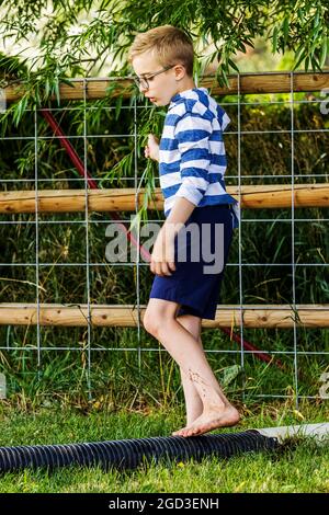 Young boy playing & balancing on drainage pipe in grassy yard Stock Photo