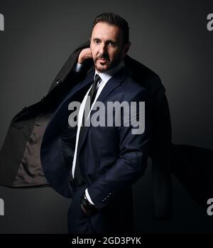 Portrait of elegant bearded businessman, boss in stylish modern office suit leaving room holding his coat on shoulder Stock Photo