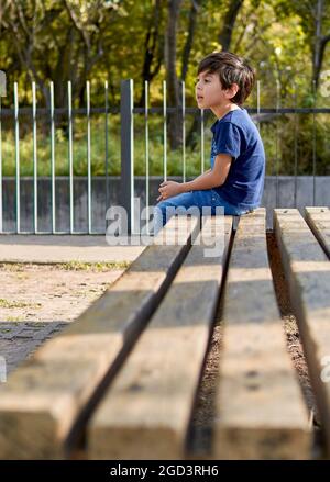 latin boy sitting in profile waiting on a square bench. vertical Stock Photo