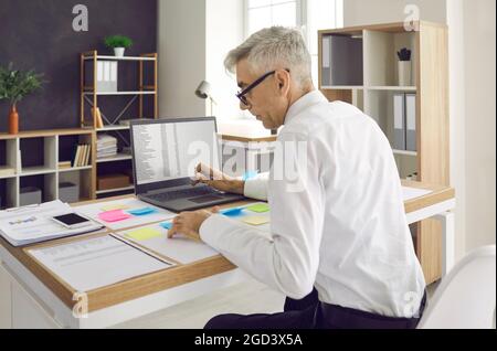 Senior man working at office desk with papers, notes and laptop computer Stock Photo