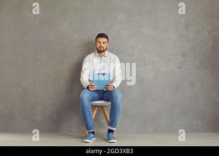 The only job candidate sitting on a chair and holding a clipboard with his resume Stock Photo