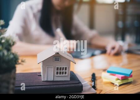 Architect woman using a digital tablet application to hand-draw a design house with a model on a wooden desk. Property idea in real estate Stock Photo