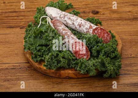 Spanish Fuet sausage with salad leaves over wooden background Stock Photo